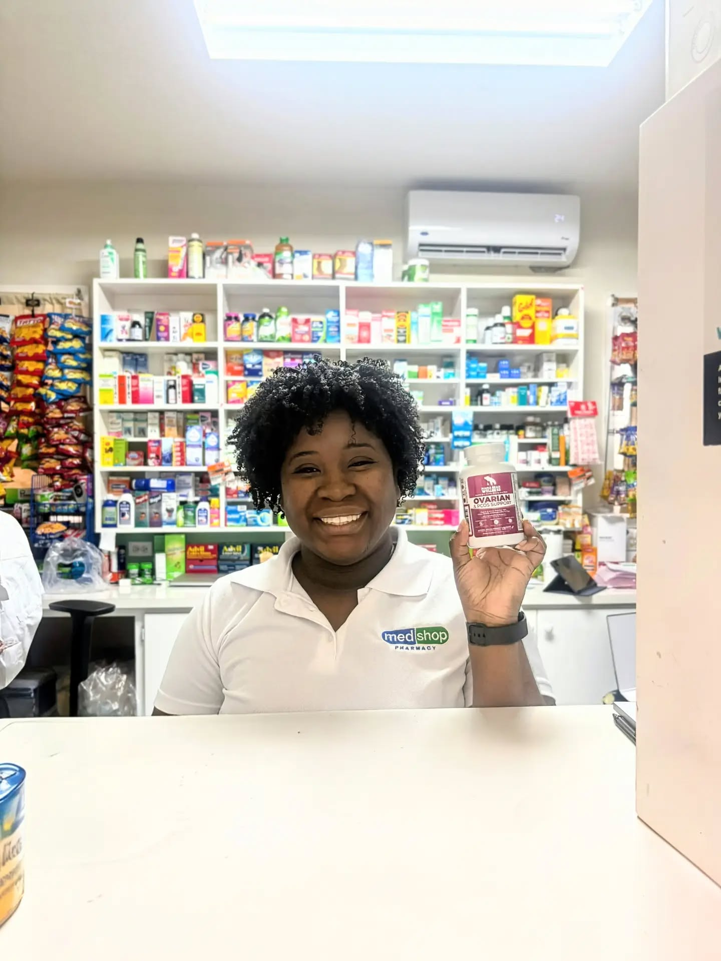 Smiling Medshop Pharmacy staff member holding a bottle of Mama Bear Ovarian & PCOS Support at the pharmacy counter